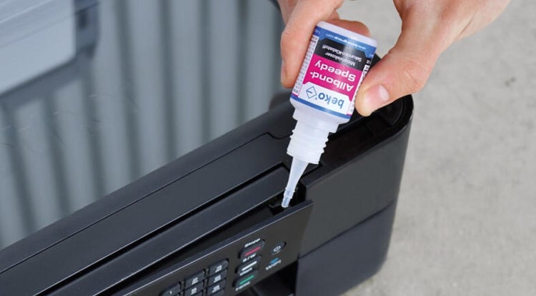 Eine Hand hält eine Flasche Beko Allbond Speedy Sekundenkleber über einen Drucker.