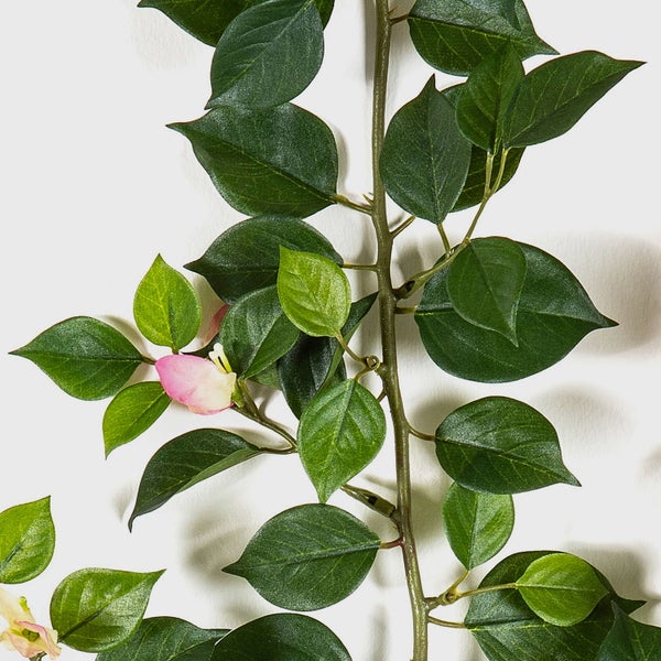 Künstliche Girlande mit grünen Blättern und einer kleinen rosa Blüte an einem braunen Stiel.