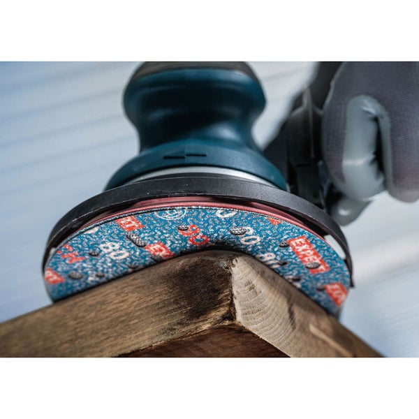 Ein Schwingschleifer mit Schleifpapier bearbeitet ein Stück Holz.