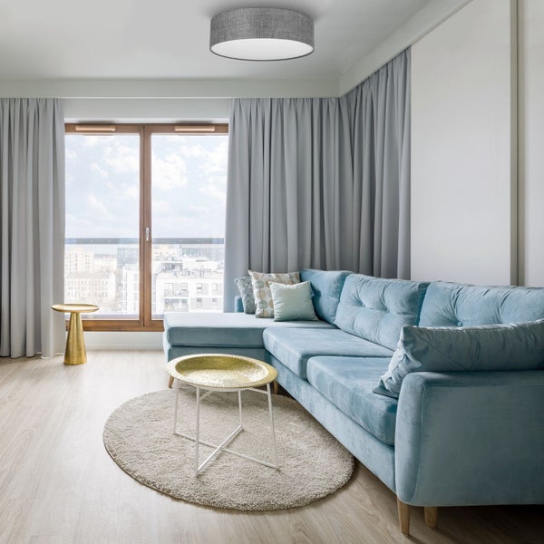 Wohnzimmer mit blauem Ecksofa, rundem Teppich und Vorhängen