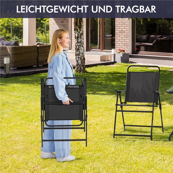 Eine Frau trägt einen leichten, zusammengeklappten Gartenstuhl auf einem Rasen, daneben steht ein aufgestellter Klappstuhl aus Textil und Metall.
