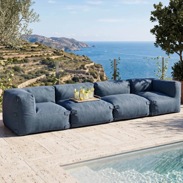Modulares Outdoor-Lounge-Sofa in Blau auf einer hellen Steinterrasse am Pool mit Blick auf die Küste.