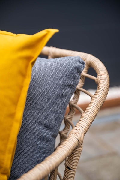 Nahaufnahme einer Rückenlehne eines Gartenstuhls aus Kunststoffgeflecht mit einem grauen und einem gelben Kissen.