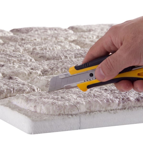 Hand schneidet mit einem Cuttermesser eine Isolierplatte in Steinoptik