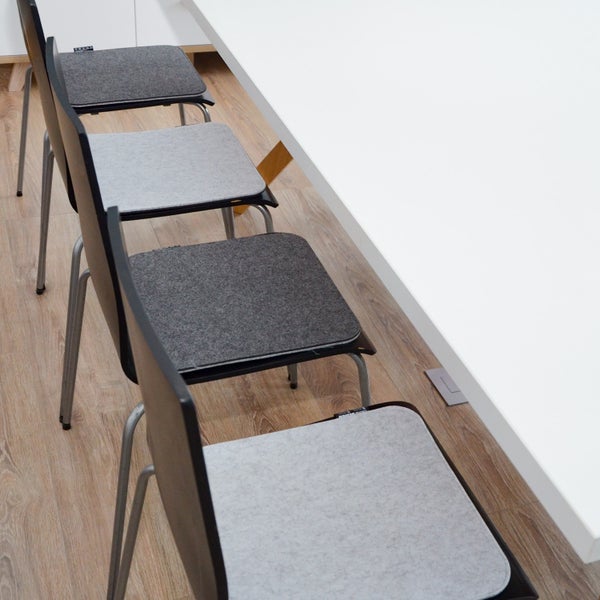 Mehrere Stühle mit Filzauflagen am weißen Tisch in einem hellen Raum mit Holzoptik Bodenbelag