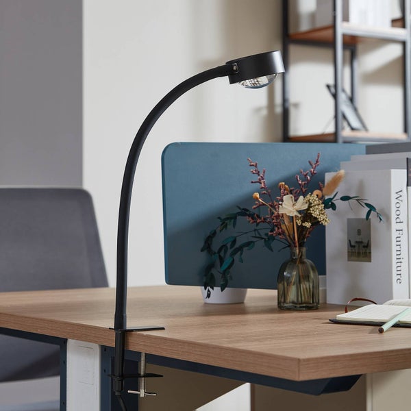 Schreibtischszene mit einer schwarzen Klemmleuchte, die auf einem Holztisch befestigt ist