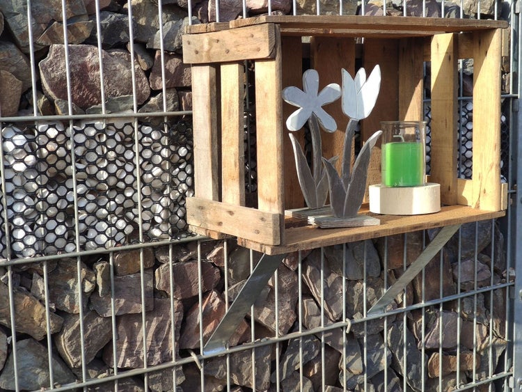 Dekoratives Holzkästchen mit Kerze und Holzblumen an einem Gabionenzaun