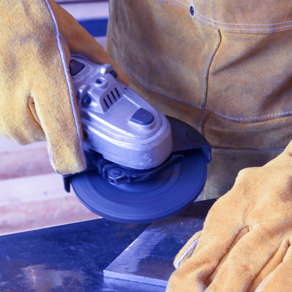 Winkelschleifer in Betrieb bei der Metallbearbeitung, geführt von Händen in robusten Leder-Schutzhandschuhen.