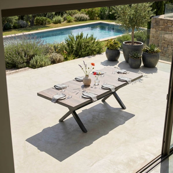 Rechteckiger Gartentisch mit Holzoptik-Platte und schwarzem X-Gestell aus Metall auf einer Terrasse neben einem Pool.