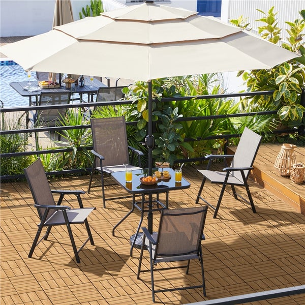 Helles Gartenmöbel-Set auf Holzterrasse mit großem gestuftem beigem Sonnenschirm, schwarzem Metalltisch mit Glasplatte und vier grauen Klappstühlen.