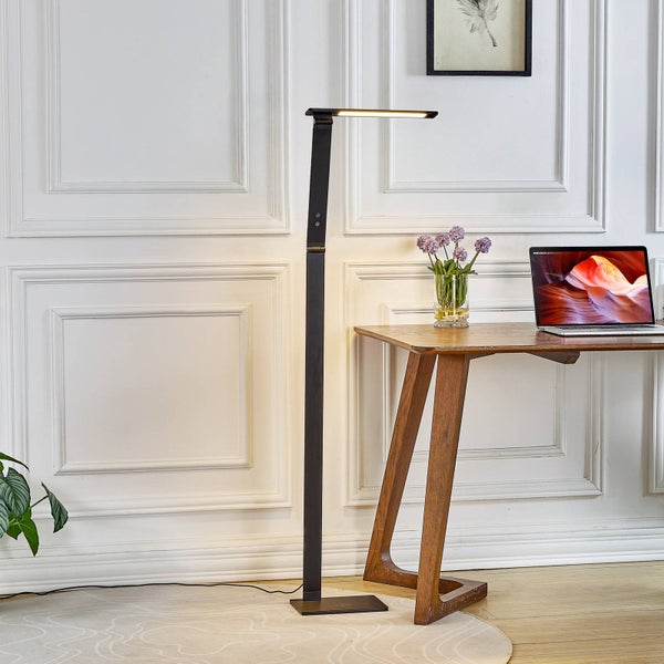 Moderne schwarze Stehleuchte mit schlankem Design neben einem Holzschreibtisch in einem hellen Raum mit Wandverzierungen.