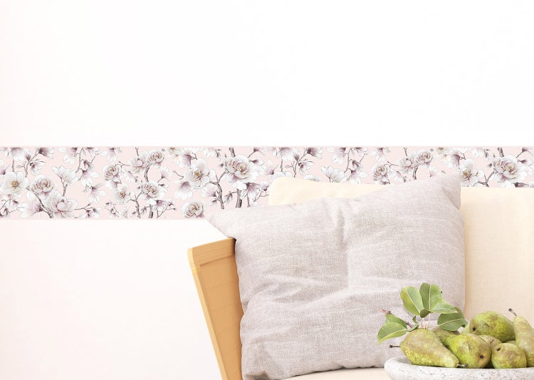 Tapetenbordüre mit floralem Magnolienmuster an einer weißen Wand hinter einem Sessel mit Kissen.