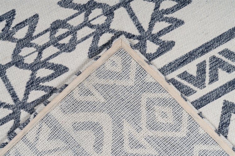 Nahaufnahme eines Teppichs mit blauem geometrischem Muster und umgeknickter Ecke, die die strukturierte Rückseite zeigt.