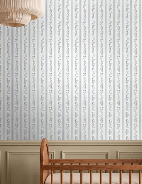 Tapete mit vertikalen Streifen und floralen Motiven in einem Kinderzimmer mit Gitterbett aus Holz und Wandpaneelen.