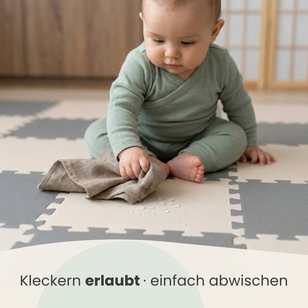 Ein Baby sitzt auf einer Puzzlematte aus Schaumstoff und wischt verschüttetes Wasser mit einem Tuch von der pflegeleichten Oberfläche ab.