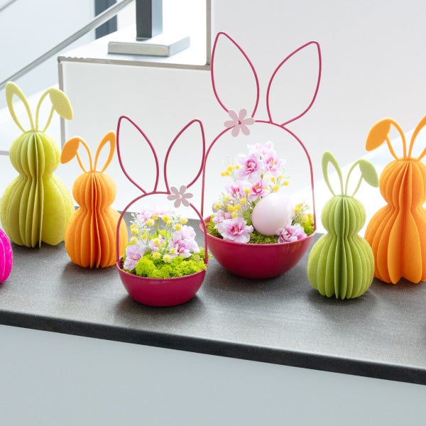 Osterdekoration bestehend aus Filzhasen und runden Metallschalen mit Hasenohren, Blumen und Ostereiern als festliche Tischdekoration.