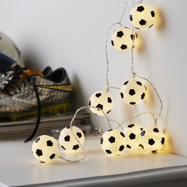 Dekorative Lichterkette mit Fußballmotiven, platziert auf einer Ablage mit einem Fußballschuh im Hintergrund.