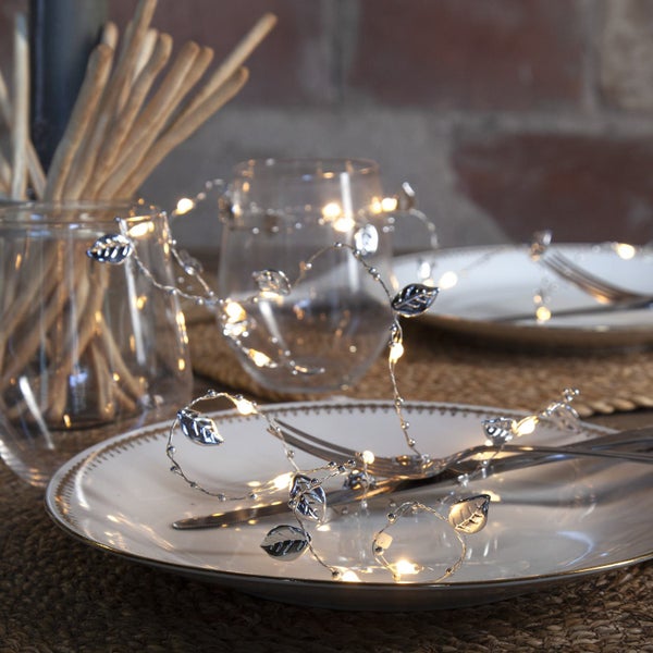 Dekorativer Tisch mit Lichterkette und Besteck auf einem Teller