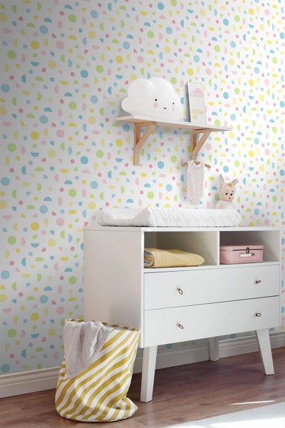 Helles Kinderzimmer mit bunter Mustertapete aus geometrischen Formen, weißer Wickelkommode und Wandregal aus Holz.