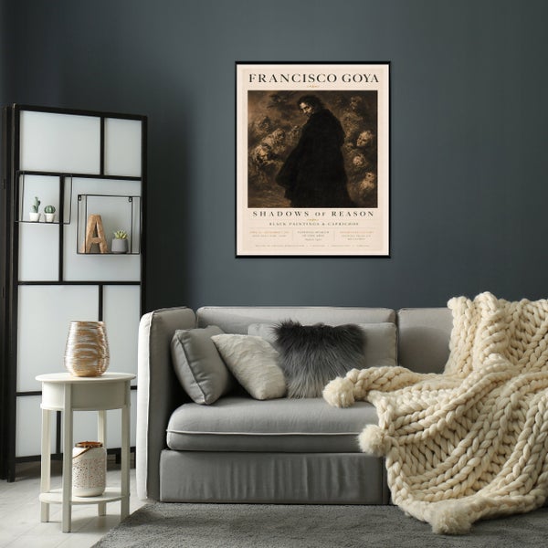 Wohnzimmer mit grauem Sofa, grob gestrickter Decke, kleinem Beistelltisch und gerahmtem Francisco Goya Kunstdruck an einer dunklen Wand.