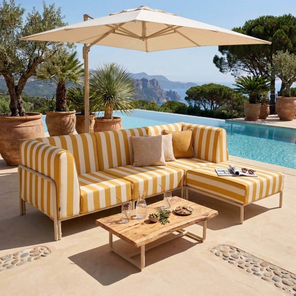 Moderne Outdoor-Lounge mit gelb-weiß gestreiftem Sofa, Holztisch und großem Ampelschirm auf einer Terrasse am Pool mit Meerblick.