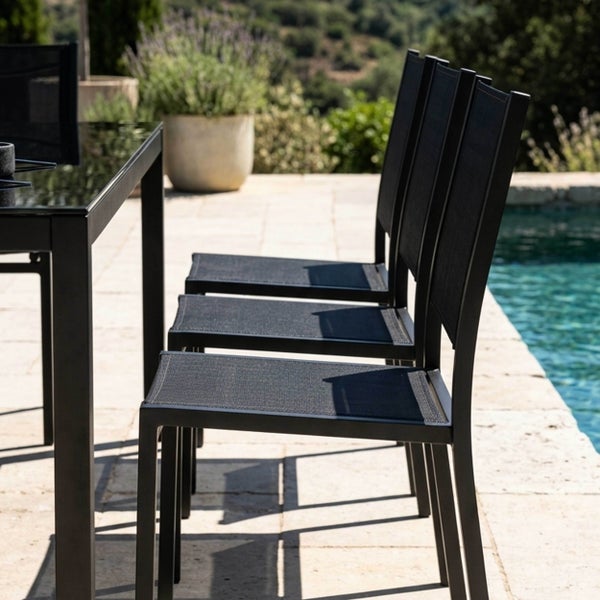 Moderne Gartenstühle mit schwarzem Metallgestell und Textilbespannung auf einer Terrasse am Pool neben einem Esstisch.