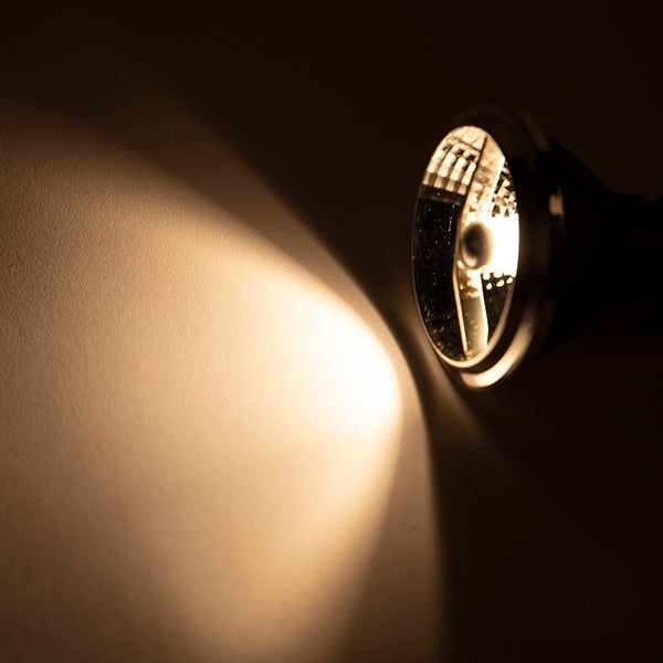 Eingeschaltete LED-Reflektorlampe mit warmweißem Lichtkegel auf einer Oberfläche.