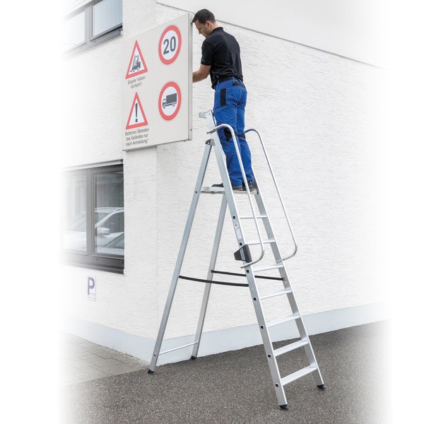 Mann auf einer Aluminium-Sicherheitsleiter, der ein Schild mit Verkehrshinweisen befestigt.