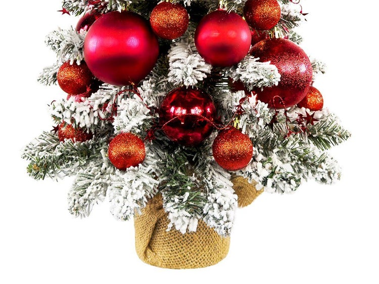 Künstlicher Weihnachtsbaum mit Kunstschnee dekoriert mit roten Weihnachtskugeln in einem Jutesack