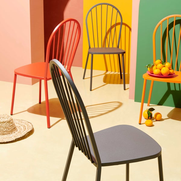 Moderner Gartenstuhl aus Metall im Windsor-Stil in verschiedenen Farben, arrangiert in einer hellen Szene mit Strohhut und Orangen.