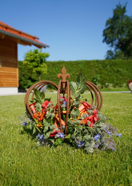 Dekorative Krone aus Metall mit Rost-Optik als Pflanzgefäß oder Gartendekoration auf einem Rasen platziert.