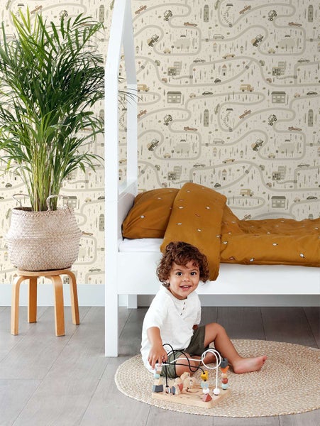 Kinderspielzimmer mit heller Mustertapete mit Auto und Straßenmotiv, weißem Kinderbett, Bettwäsche und spielendem Kleinkind auf rundem Teppich.