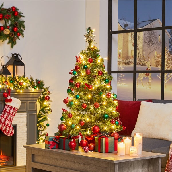 Dekorierter Weihnachtsbaum auf einem Tisch in einem Wohnzimmer mit Kamin und Blick aus dem Fenster auf eine verschneite Landschaft.