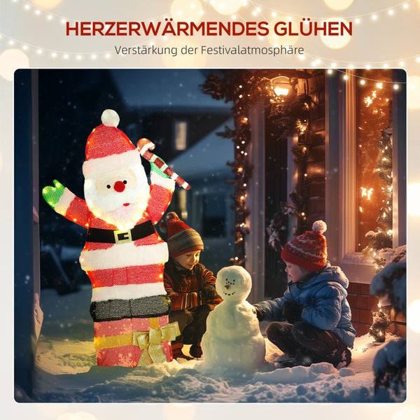 Beleuchtete Weihnachtsmann-Figur auf einem Geschenkkarton im Schnee neben Kindern, die einen Schneemann vor einem Haus bauen.