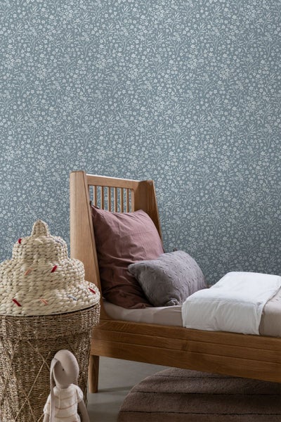 Kinderzimmer mit floral gemusterter Tapete, einem Holzbett mit Kissen und einem dekorativen geflochtenen Korb.