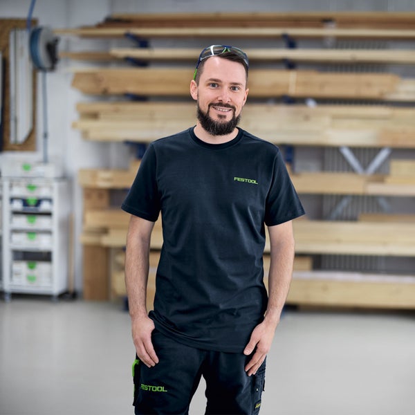 Mann mit Festool T-Shirt und Hose in Werkstatt mit Holzregal