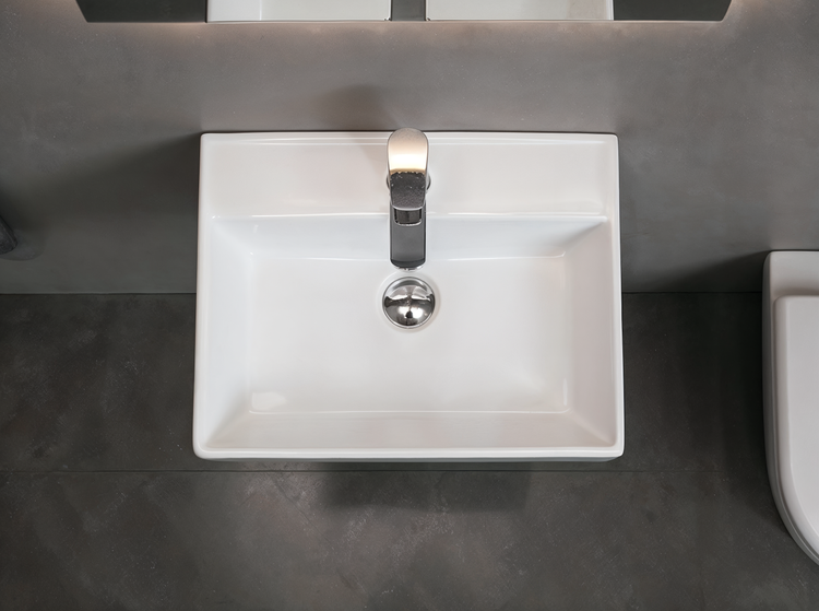 Rechteckiges Waschbecken aus Keramik mit verchromter Armatur in einem modernen Badezimmer mit Wand und Boden in Betonoptik.