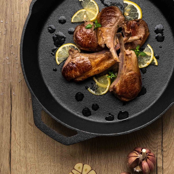 Lammkoteletts mit Zitrone und Knoblauch in einer schwarzen Bratpfanne auf einem Holztisch