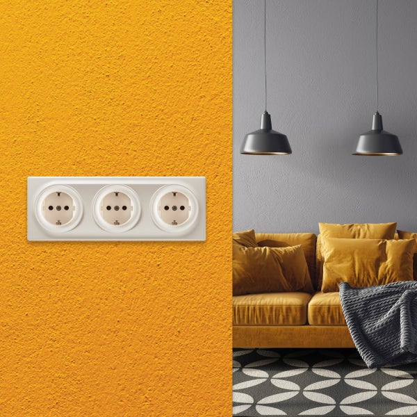 Dreifach Steckdose unterputz an einer strukturierten Wand in einem modern eingerichteten Wohnzimmer mit Sofa und Hängeleuchten.