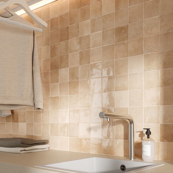 Quadratische Fliesen in Natursteinoptik an einer Wand im Badezimmer mit Waschbecken, Wasserhahn und Handtüchern.