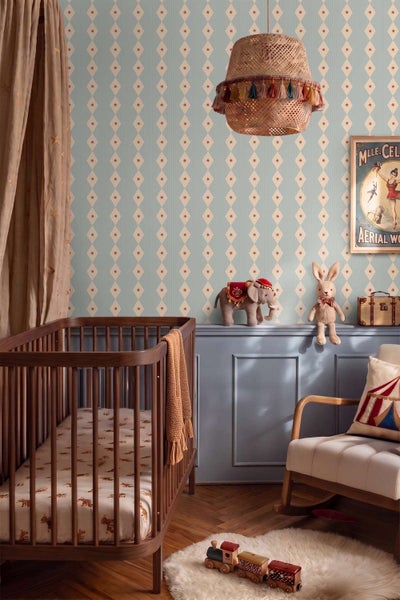 Kinderzimmer mit Zirkus Motiv Vliestapete, Holzgitterbett, Schaukelstuhl, geflochtener Lampe und Holzspielzeug auf Fischgrätparkett.