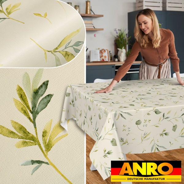 Tischdecke mit grünem Blättermotiv auf Holztisch in einer Küche, Detailansicht der Stoffstruktur und ANRO DEUTSCHE MANUFAKTUR Logo.