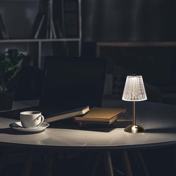 Nachttischszene mit einer Tischlampe aus Metall und Kunststoff neben Büchern, einer Tasse und einem Laptop