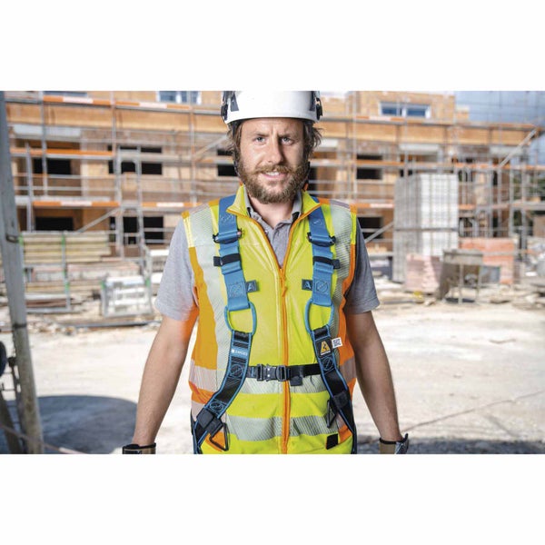 Bauarbeiter auf einer Baustelle mit weißem Schutzhelm, Warnweste und blauem Auffanggurt.