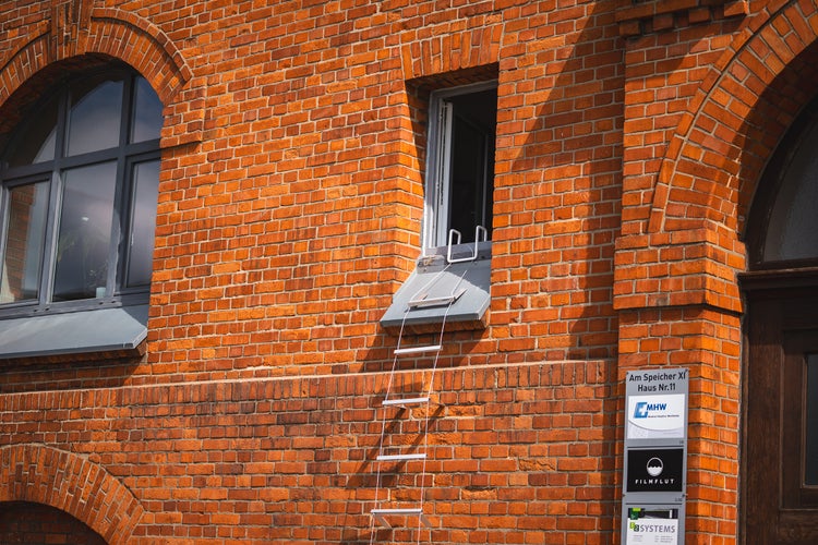 Außenansicht eines roten Backsteingebäudes mit Fenstern und einer Notleiter