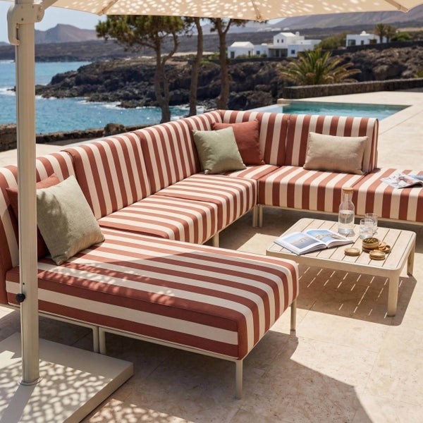 Moderne Gartenlounge mit gestreiftem Ecksofa und Couchtisch aus Holzlatten auf einer Terrasse mit Pool und Meerblick.