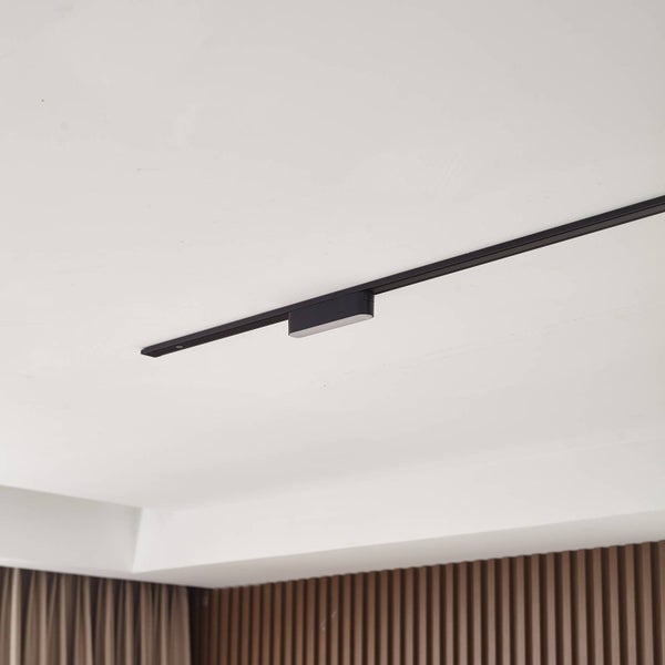Modernes schwarzes Schienensystem mit rechteckiger Leuchte an einer weißen Decke in einem minimalistischen Raum.
