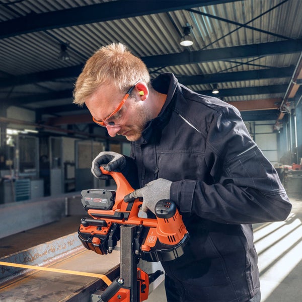 Ein Arbeiter bedient eine tragbare Bandsäge zum Schneiden von Metall, wobei er Schutzkleidung wie Schutzbrille und Handschuhe trägt.