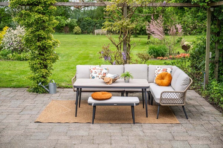 Helle, organisierte Terrasse mit einer modernen Gartenlounge aus Metall und Seilgeflecht, bestehend aus Ecksofa, Esstisch und Bank im Garten.