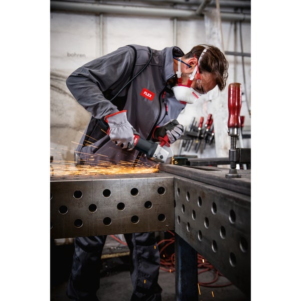 Handwerker mit Schutzausrüstung bearbeitet ein Metallwerkstück auf einem Schweißtisch mit einem Flex Winkelschleifer.